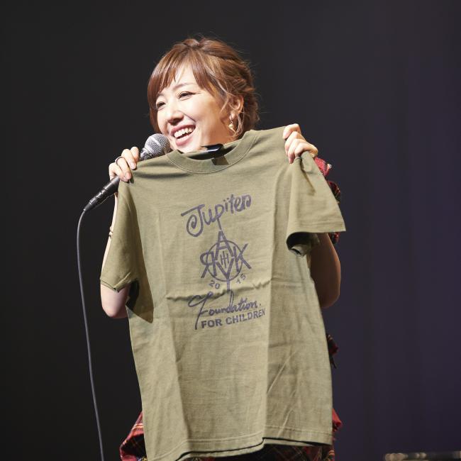 舞台でチャリティグッズのTシャツを紹介する綾香